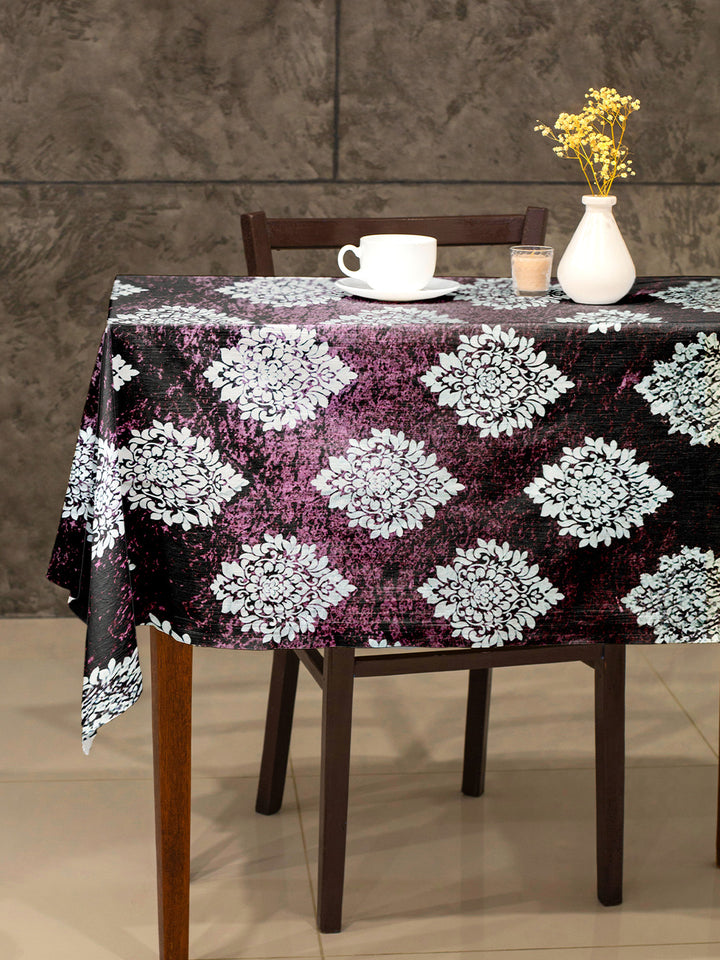 Table with a floral patterned tablecloth, cup, saucer, candle, and vase against a stone wall.