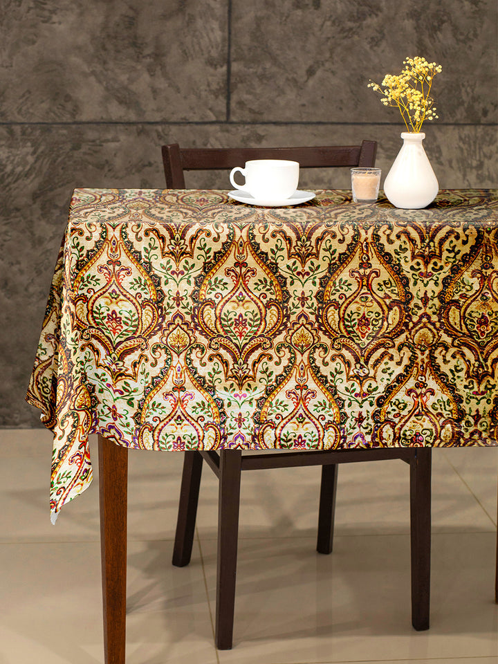 Dining table with a patterned tablecloth, cup, saucer, candle, and vase against a gray wall.