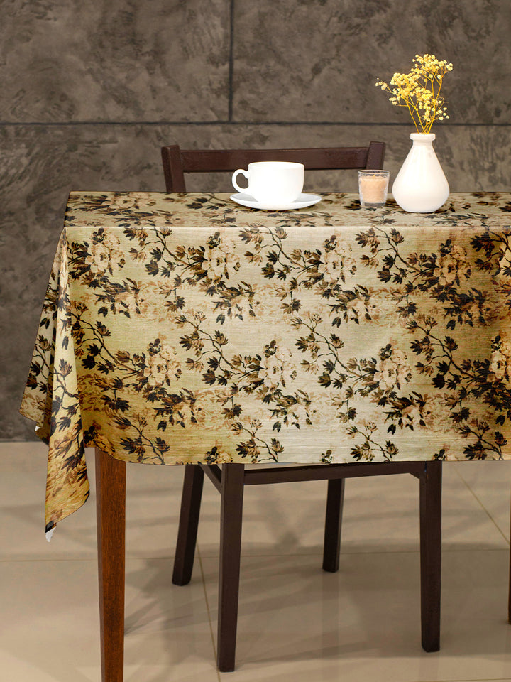 Table with floral tablecloth, cup, saucer, candle, and vase against a gray wall.