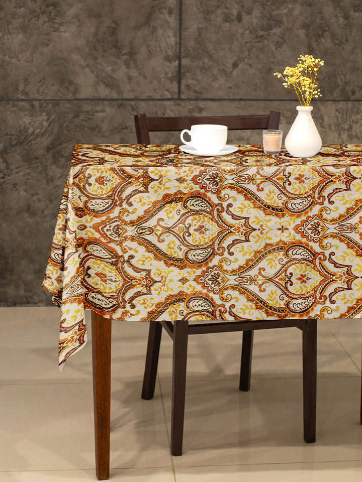 Table with a patterned tablecloth, cup, saucer, and vase against a gray wall.
