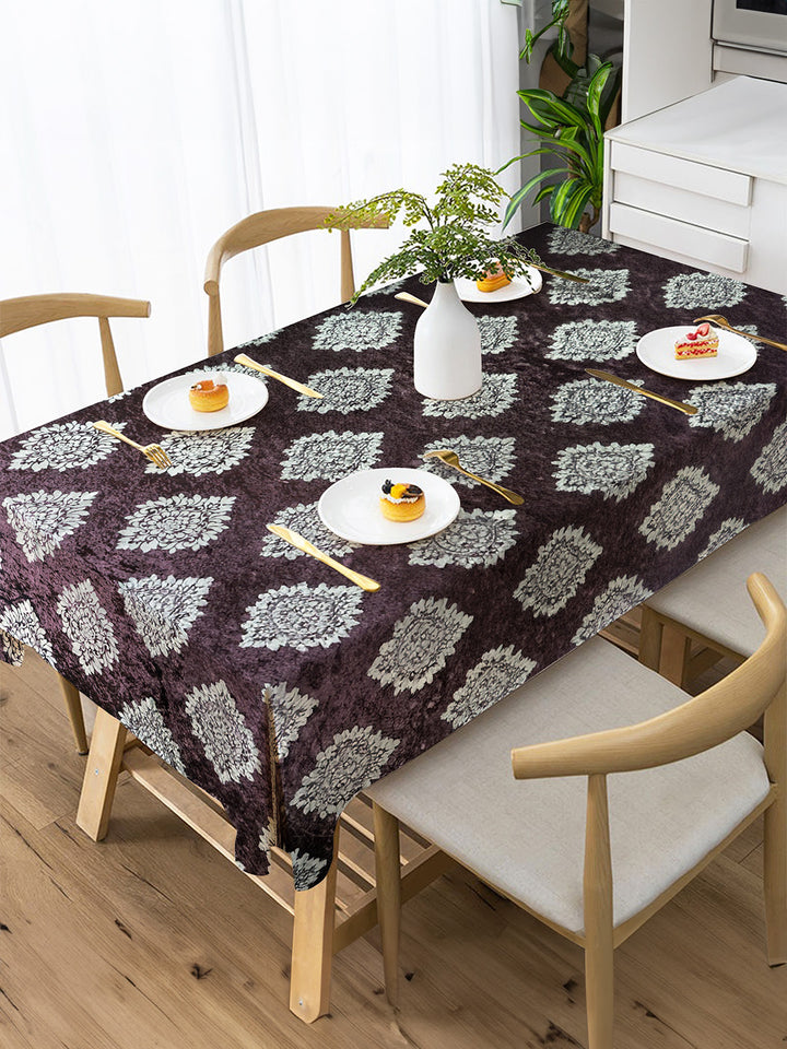 Dining table with a patterned tablecloth, plates, and cutlery in a bright room.