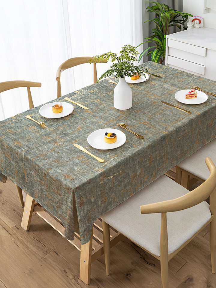 Dining table set with a patterned tablecloth, plates, and cutlery in a bright room.