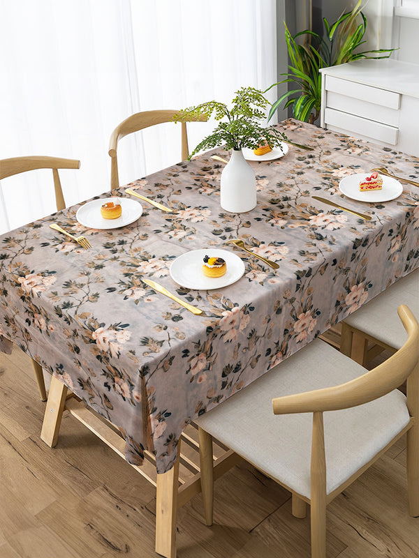 Dining table set with floral tablecloth, plates, and chairs in a bright room.