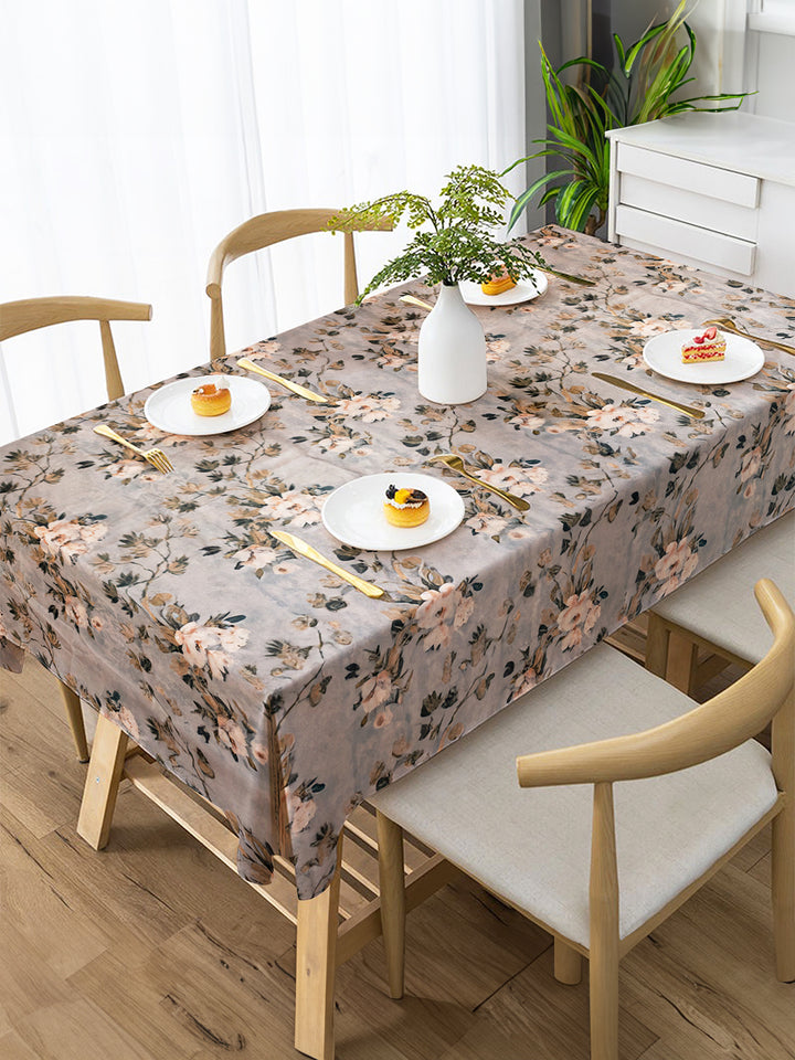 Dining table set with floral tablecloth, plates, and chairs in a bright room.