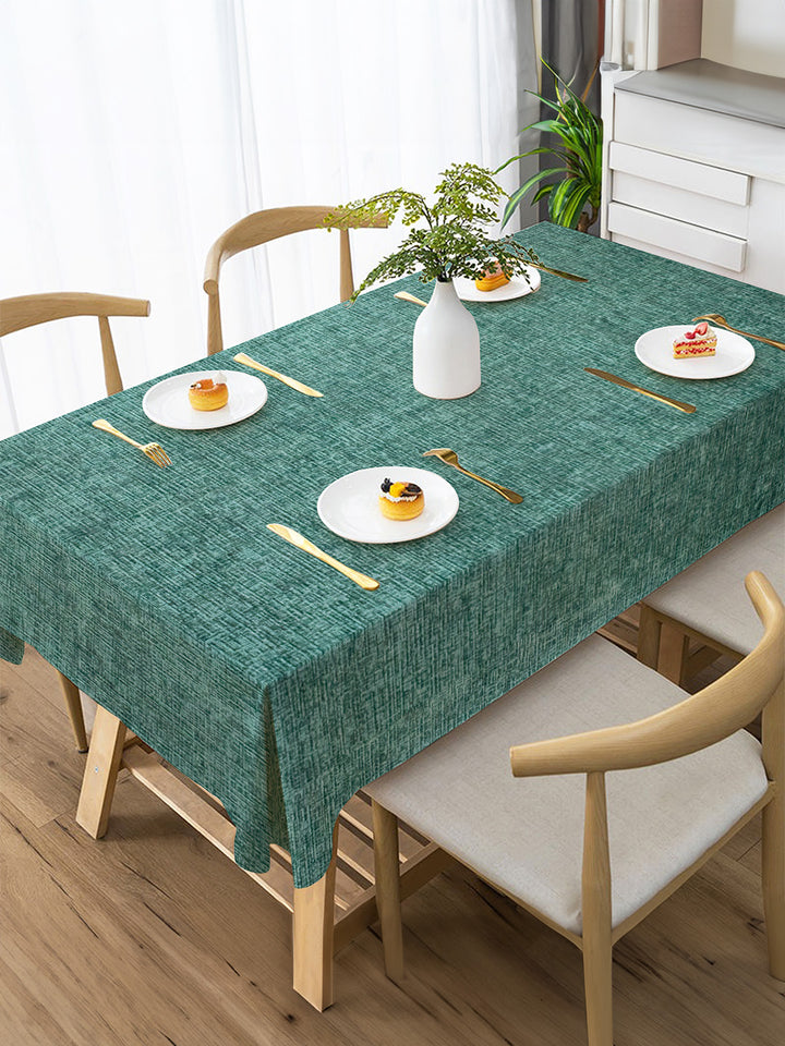 Dining table with a green tablecloth, plates, and cutlery in a bright room.