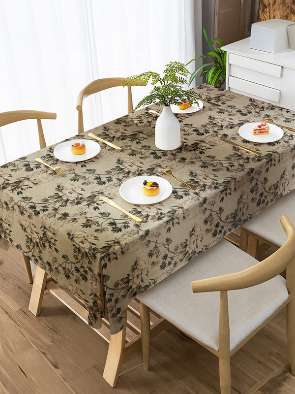 Dining table set with floral tablecloth, plates, and chairs in a bright room.