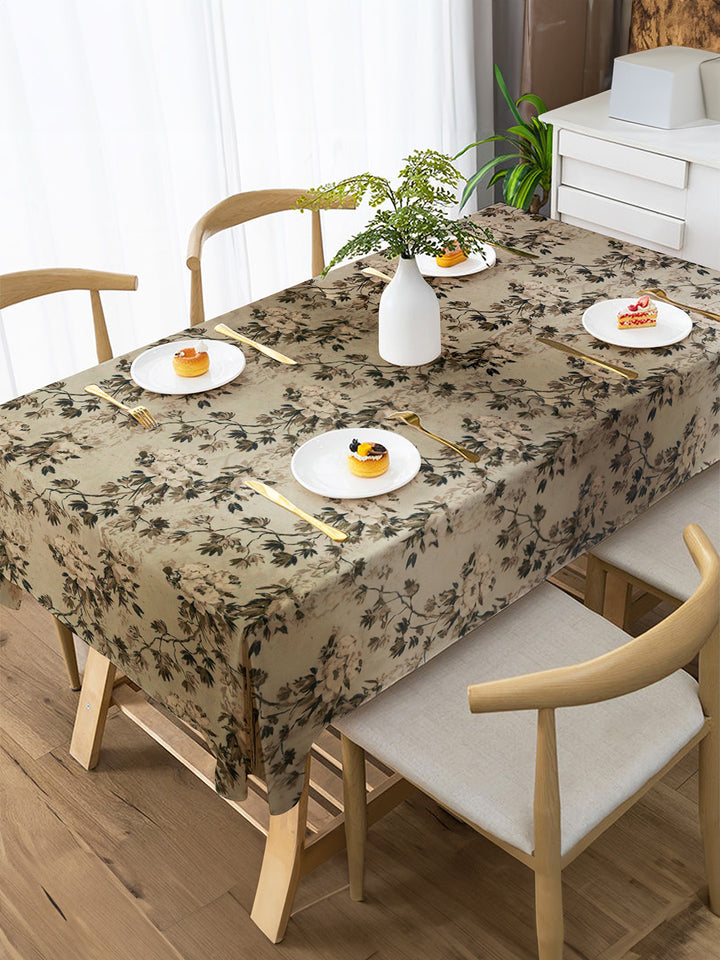 Dining table set with floral tablecloth, plates, and chairs in a bright room.