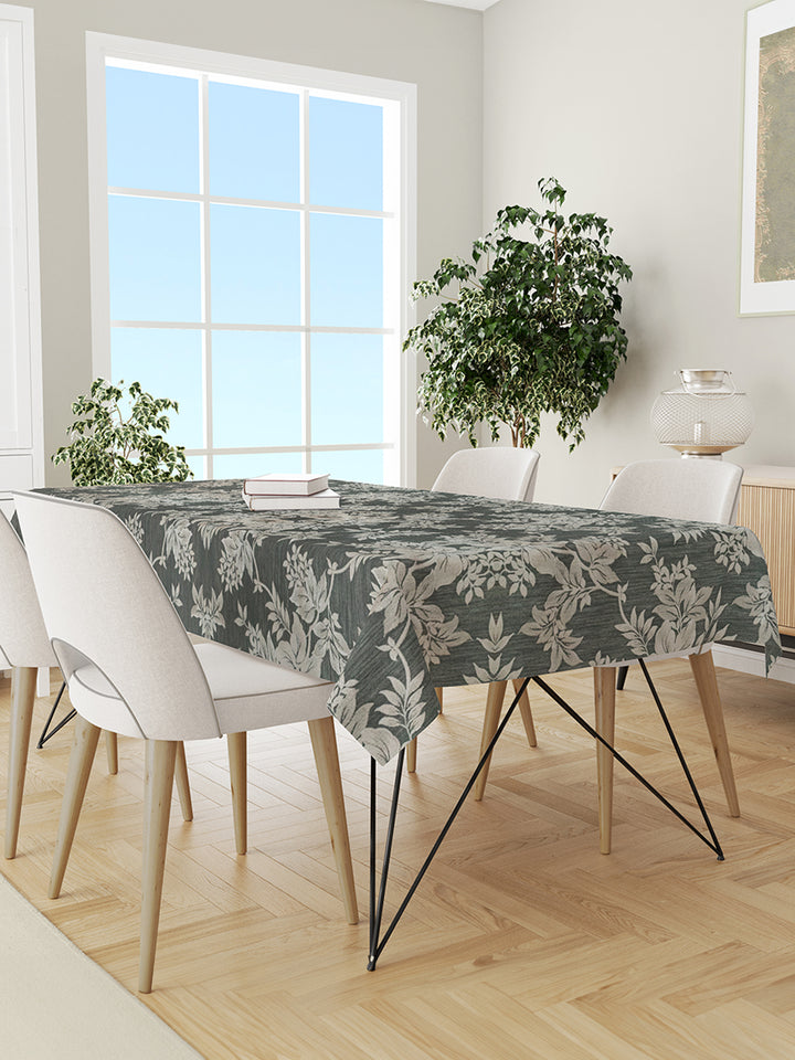 Dining room with a table covered by a floral-patterned tablecloth, white chairs, and plants.