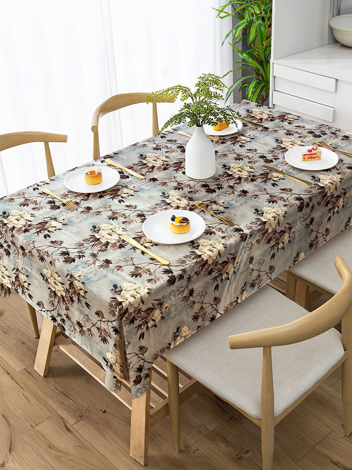 Dining table set with a floral tablecloth, plates, and cutlery on a wooden floor.