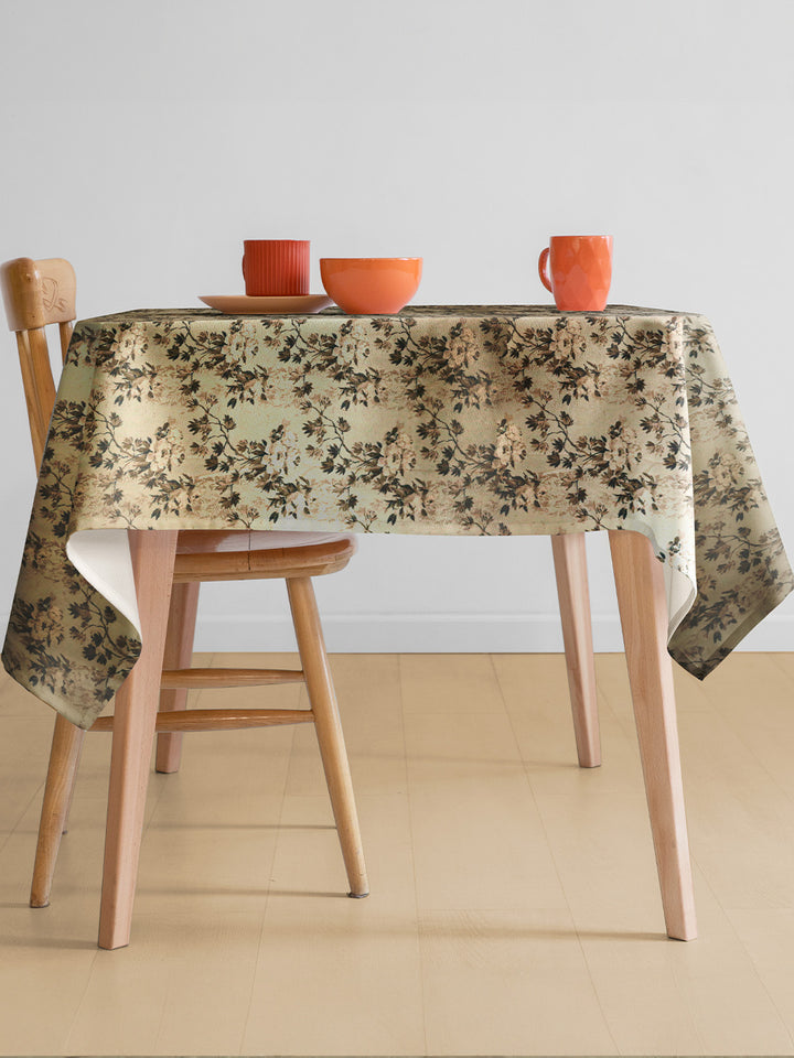 Table with floral tablecloth, wooden chairs, and colorful cups on a neutral background