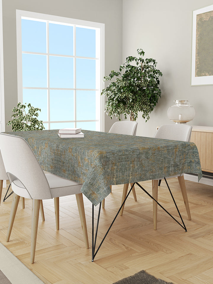 Dining room with a table covered by a green patterned tablecloth, white chairs, and plants.