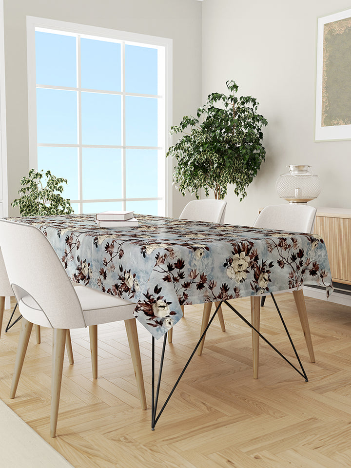 Dining room with a table covered by a floral tablecloth, chairs, and plants.