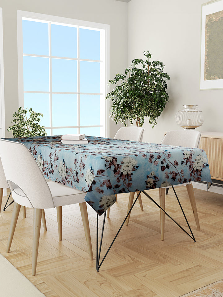 Dining room with a floral tablecloth on a table, white chairs, and plants.