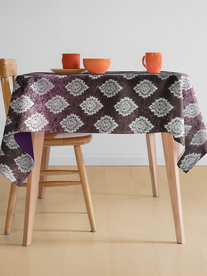 Table with a patterned tablecloth, wooden chairs, and orange cups on a plain background