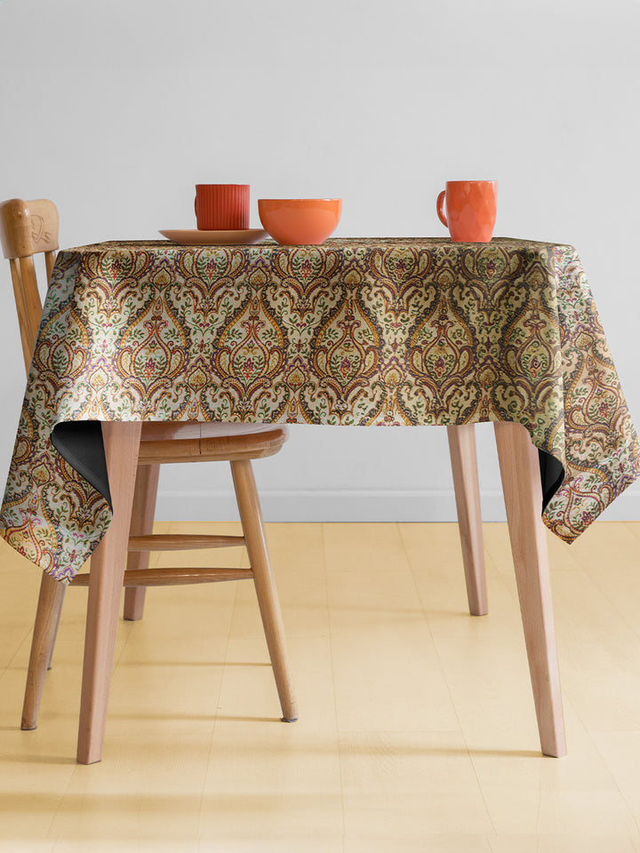 Table with a patterned tablecloth and wooden chairs on a light background