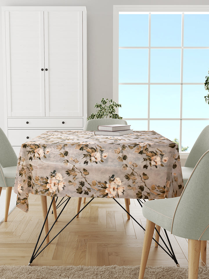 Dining room with a floral tablecloth on a table, chairs, and a window in the background.