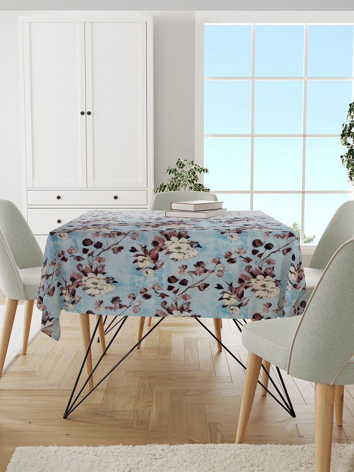 Dining room with a floral tablecloth on a table, white chairs, and a large window.