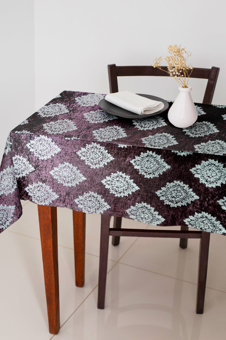 Round table with a patterned tablecloth, chair, and decorative items on a tiled floor.
