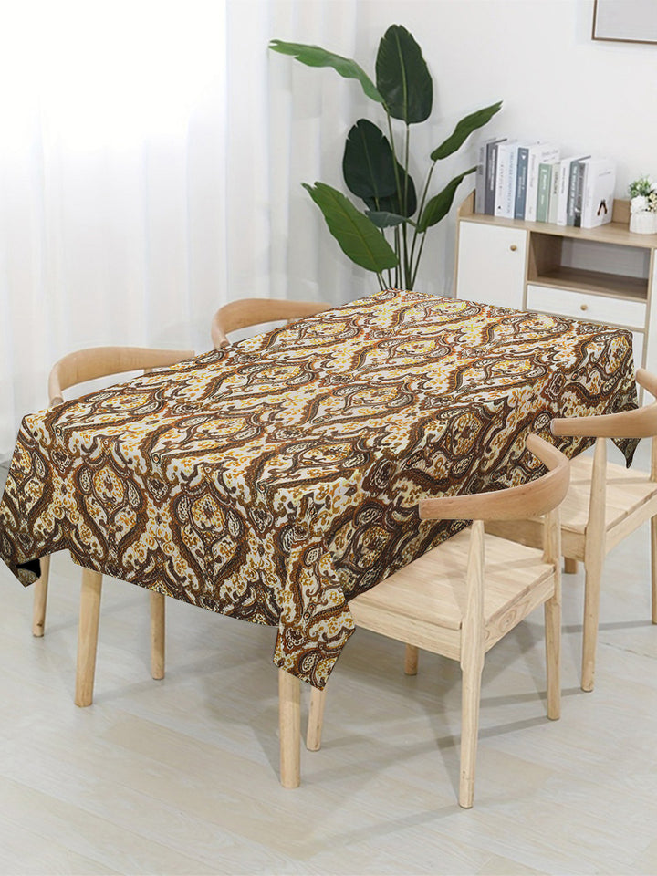 Dining table with a patterned tablecloth in a room with a plant and shelves.