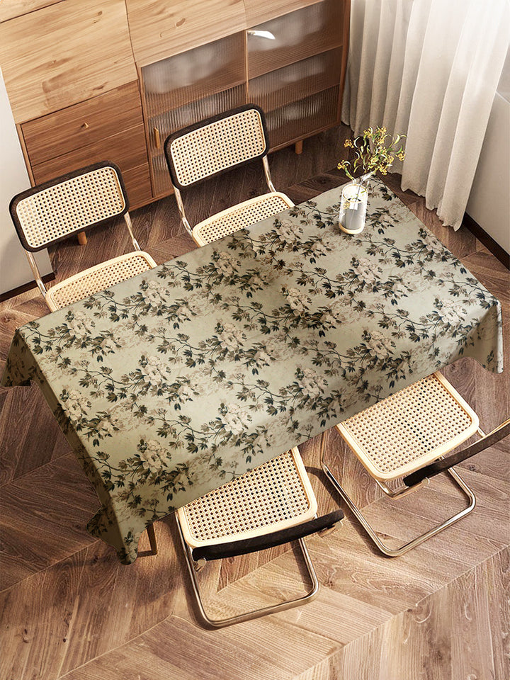 Dining table with floral tablecloth and chairs in a room with wooden floor and cabinets.
