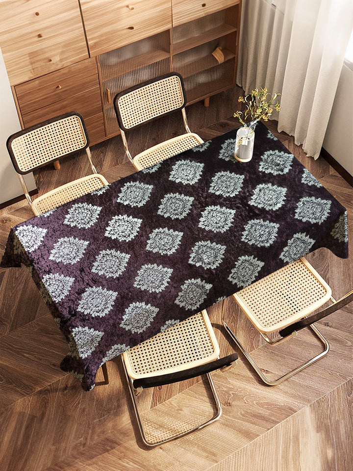 Table with a patterned tablecloth and chairs in a room with wooden flooring and furniture.