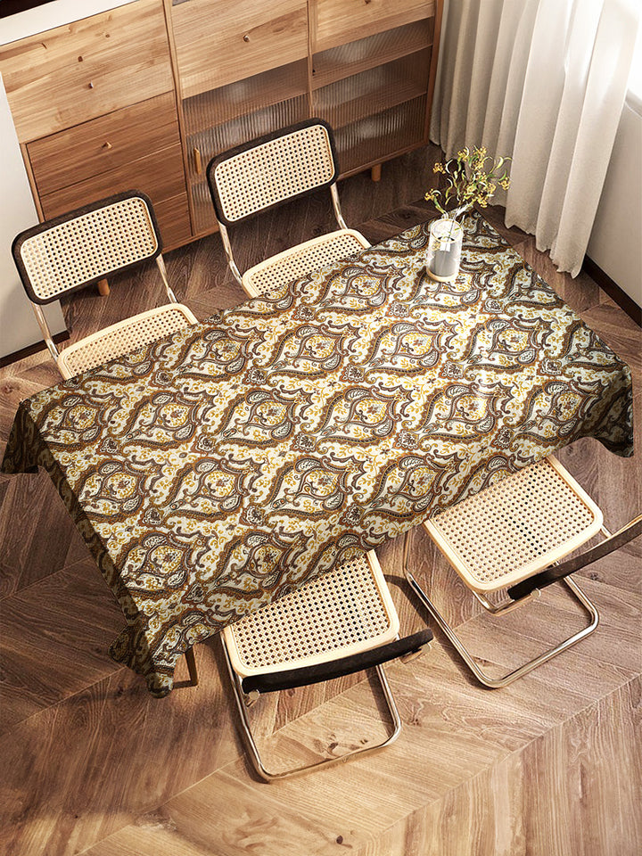 Table with a patterned tablecloth and four chairs in a room with wooden flooring and furniture.