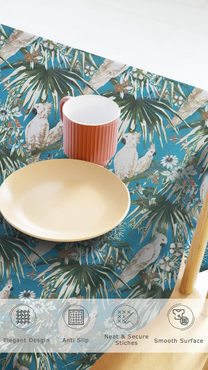 Tablecloth with tropical design featuring birds and leaves, placed on a table with a cup and bowl.
