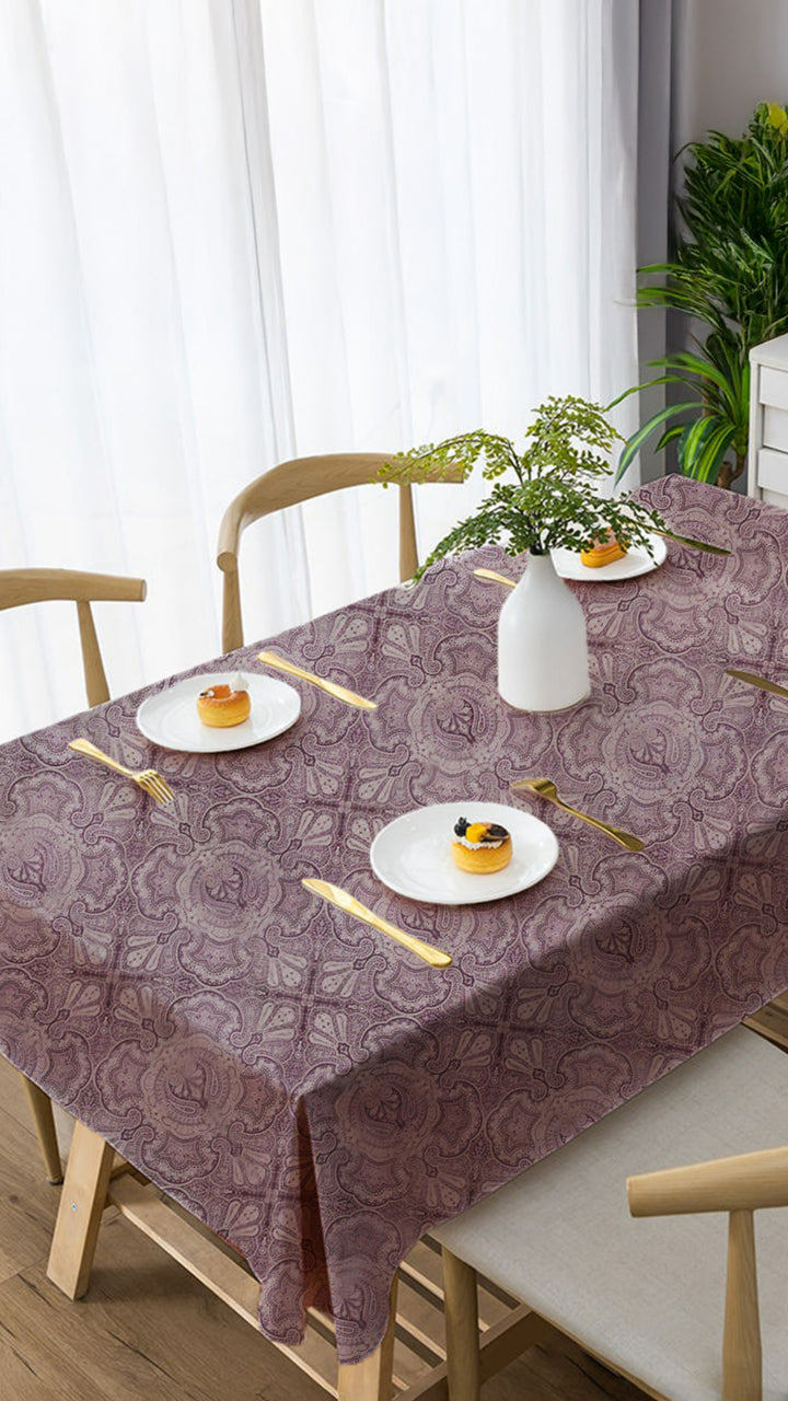 Dining table set with a patterned tablecloth, plates, cutlery, and a vase.