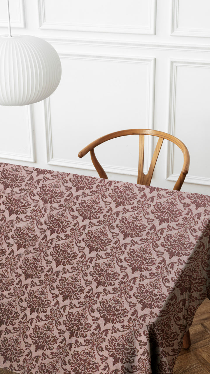 Table with a patterned tablecloth, wooden chair, and white wall with decorative molding.