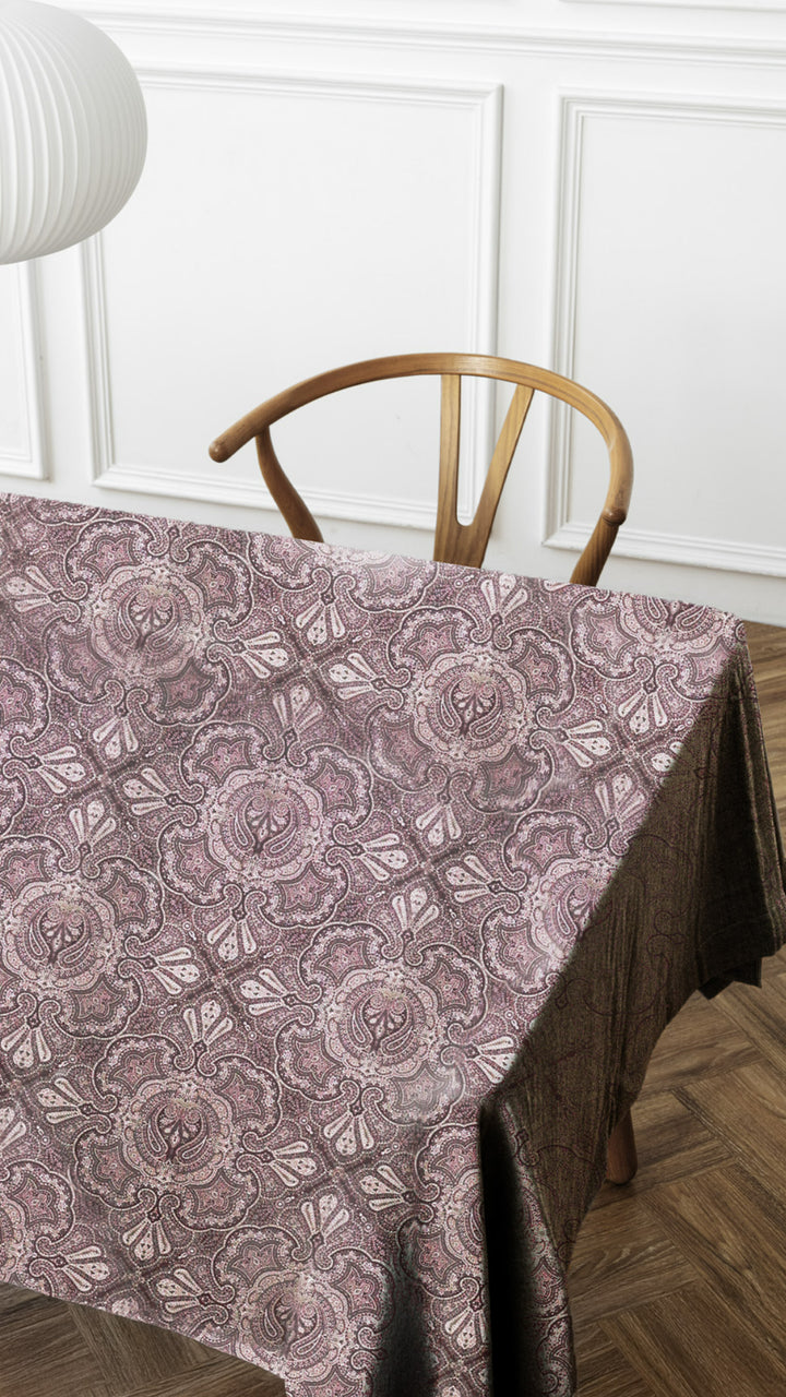 Tablecloth with a floral pattern on a wooden table against a white paneled wall.