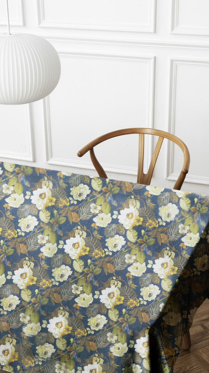 Floral-patterned tablecloth on a table with a wooden chair against a white paneled wall.
