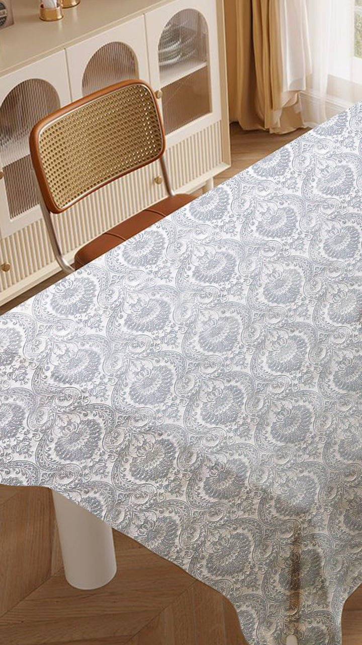 Table with a patterned tablecloth in a room with a chair and shelves.