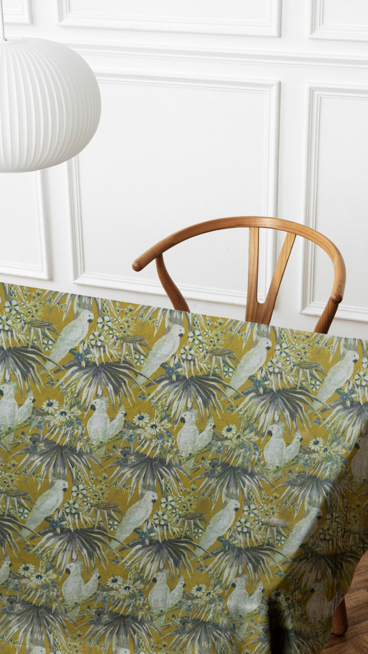 Tablecloth with parrot pattern on a table with a wooden chair against a white paneled wall.