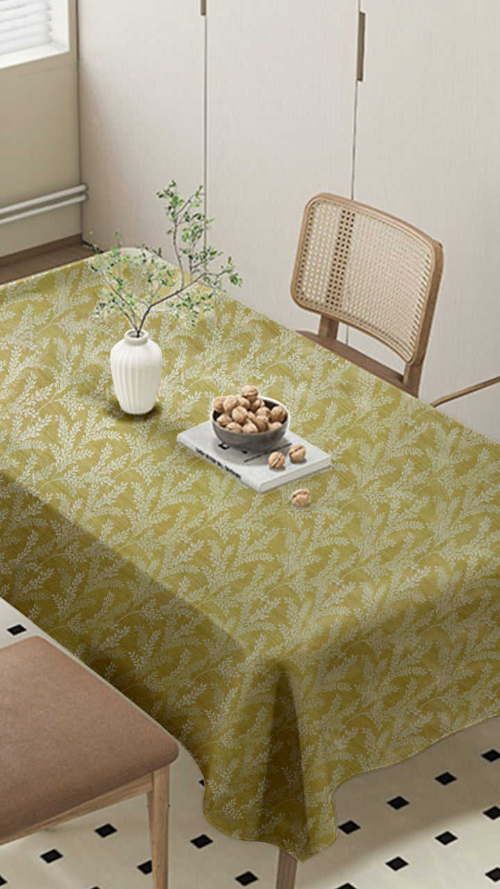Table with a green patterned tablecloth, vase, and bowl in a room.