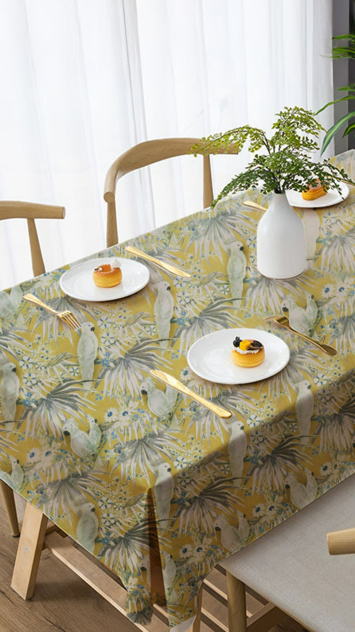 Table with floral-patterned tablecloth, plates with food, and a vase with a plant.