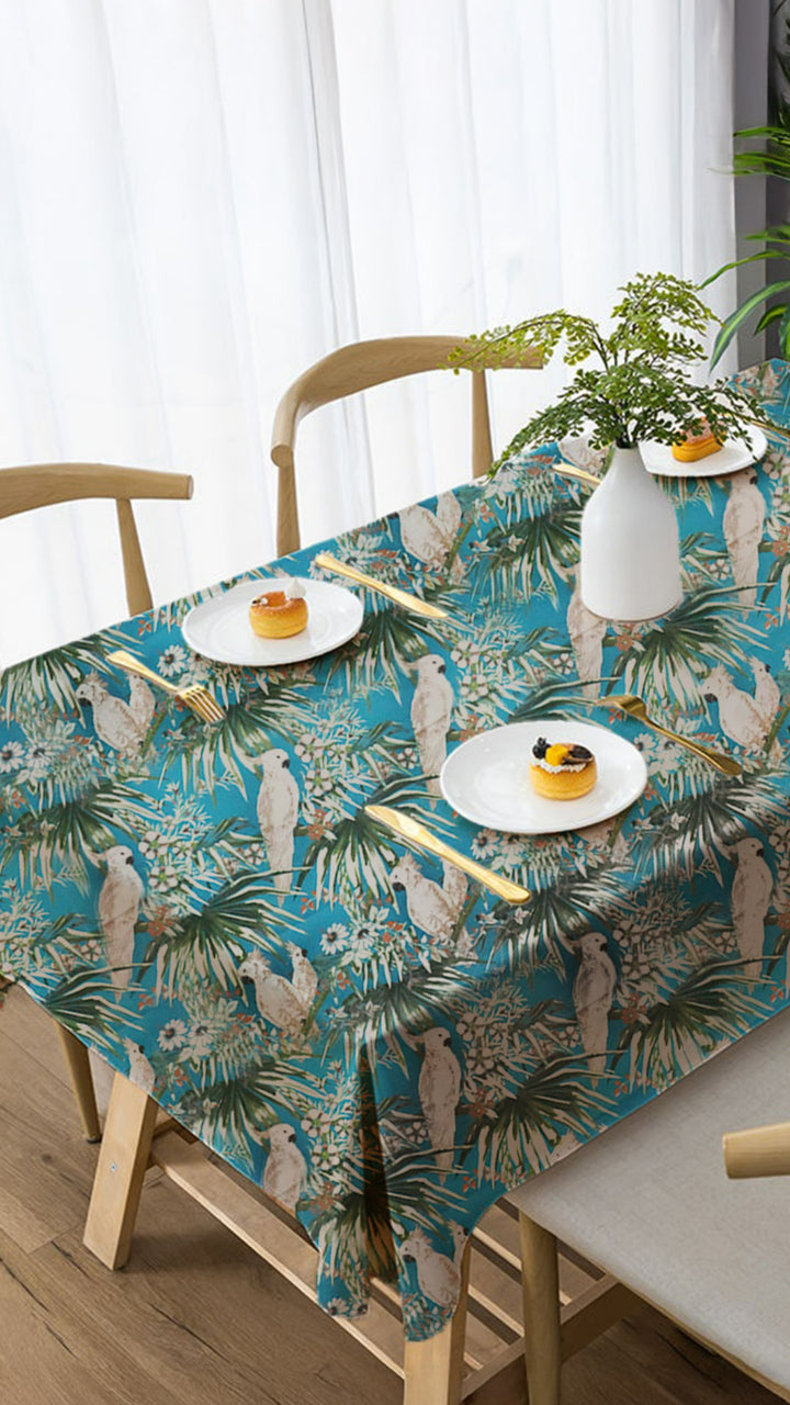 Tablecloth with tropical design on a dining table with plates and cutlery.