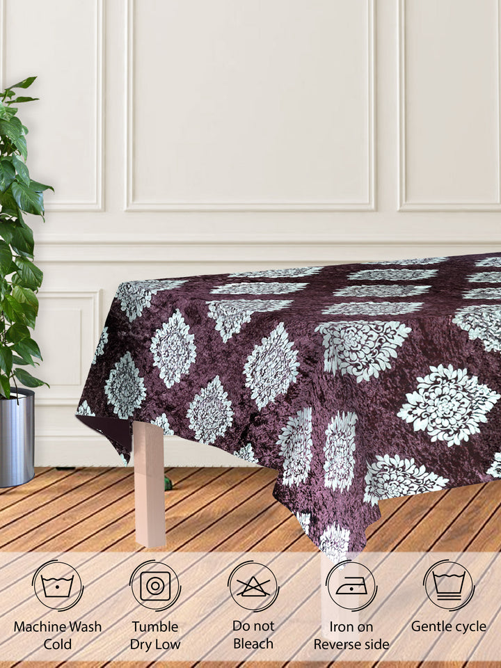 Tablecloth with a floral pattern on a wooden table against a white paneled wall.